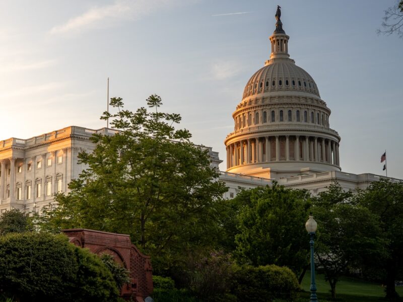 AI-generated illustration of the US Capitol building at dusk with a data center and courthouse in split foreground, representing the federal vs state AI regulation debate