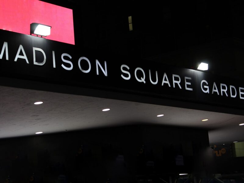 AI-generated illustration of Madison Square Garden lit in orange and blue at night with a crowd gathered outside on a New York City street