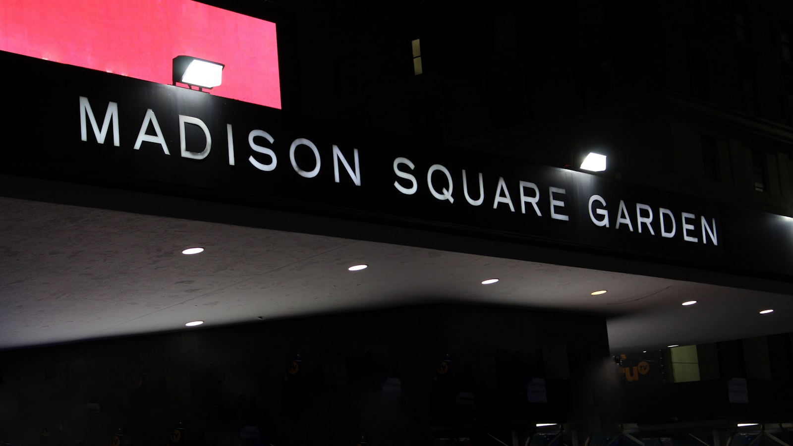 AI-generated illustration of Madison Square Garden lit in orange and blue at night with a crowd gathered outside on a New York City street