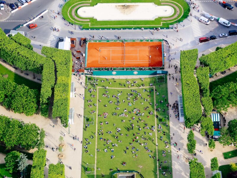 AI-generated aerial illustration of the All England Club's Centre Court surrounded by manicured grass courts on a bright summer day, Wimbledon tournament atmosphere