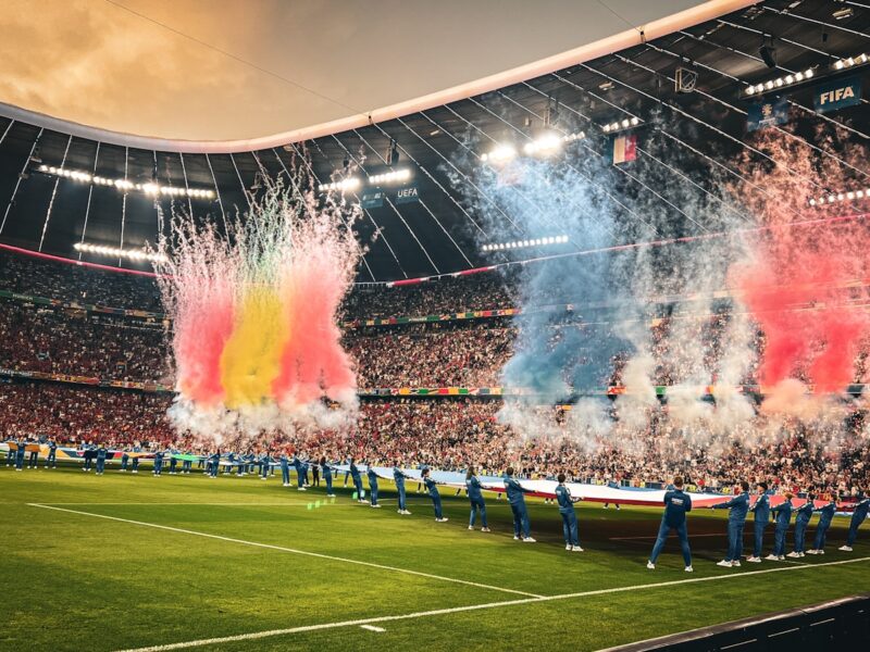 AI-generated illustration of a massive soccer stadium packed with fans from multiple nations under evening lights, representing the 2026 FIFA World Cup across three host countries