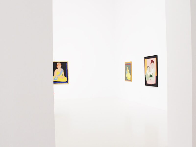 An empty gallery room with framed artworks hung on white walls above a polished floor under soft even lighting