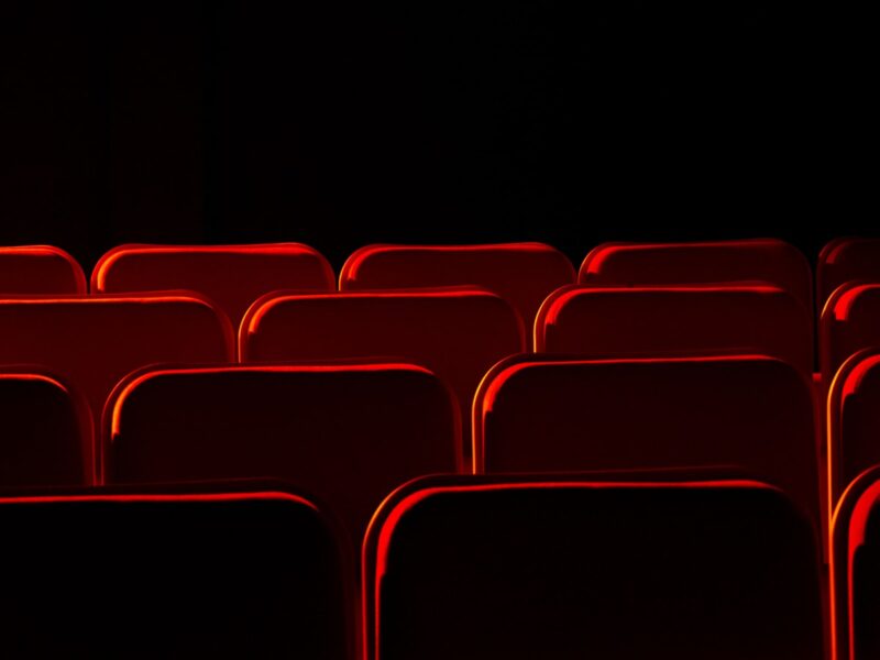 An empty cinema auditorium with rows of red seats facing a blank screen under low house lights