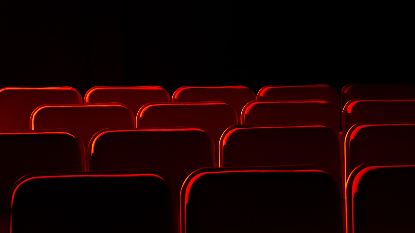 An empty cinema auditorium with rows of red seats facing a blank screen under low house lights