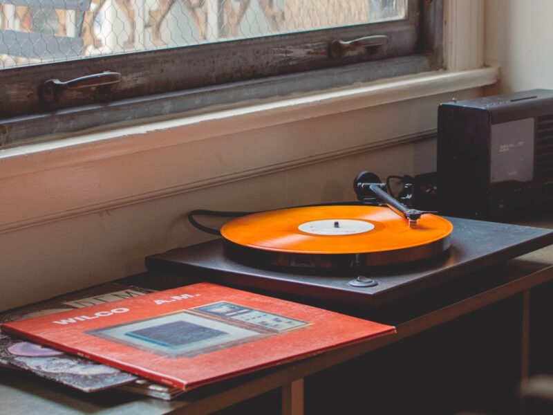 A record player on a shelf with a plain vinyl album sleeve leaning beside it in warm indoor light
