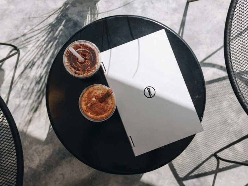 A café table holding several books, a notebook and cups of coffee with empty chairs around it in warm afternoon light