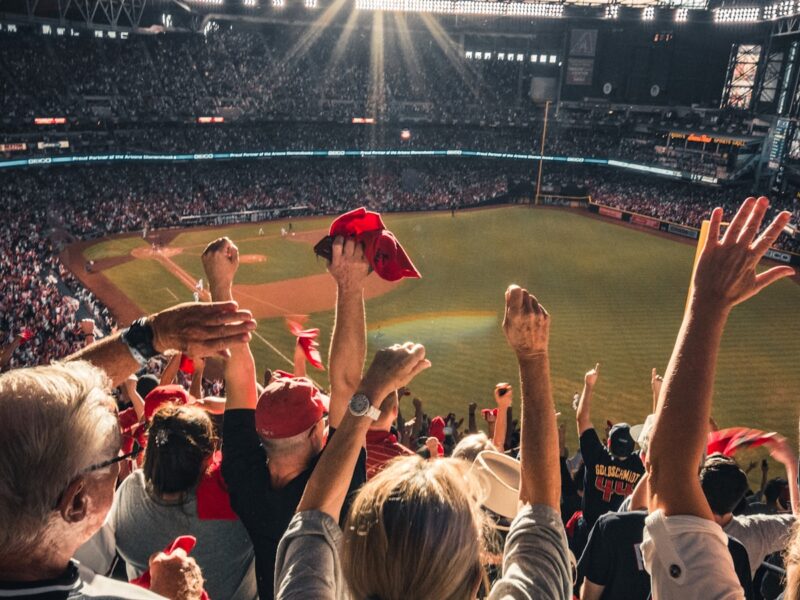 AI-generated illustration of a major league baseball stadium at dusk, pitcher's mound centered, stadium lights glowing warm amber, scoreboard visible in background