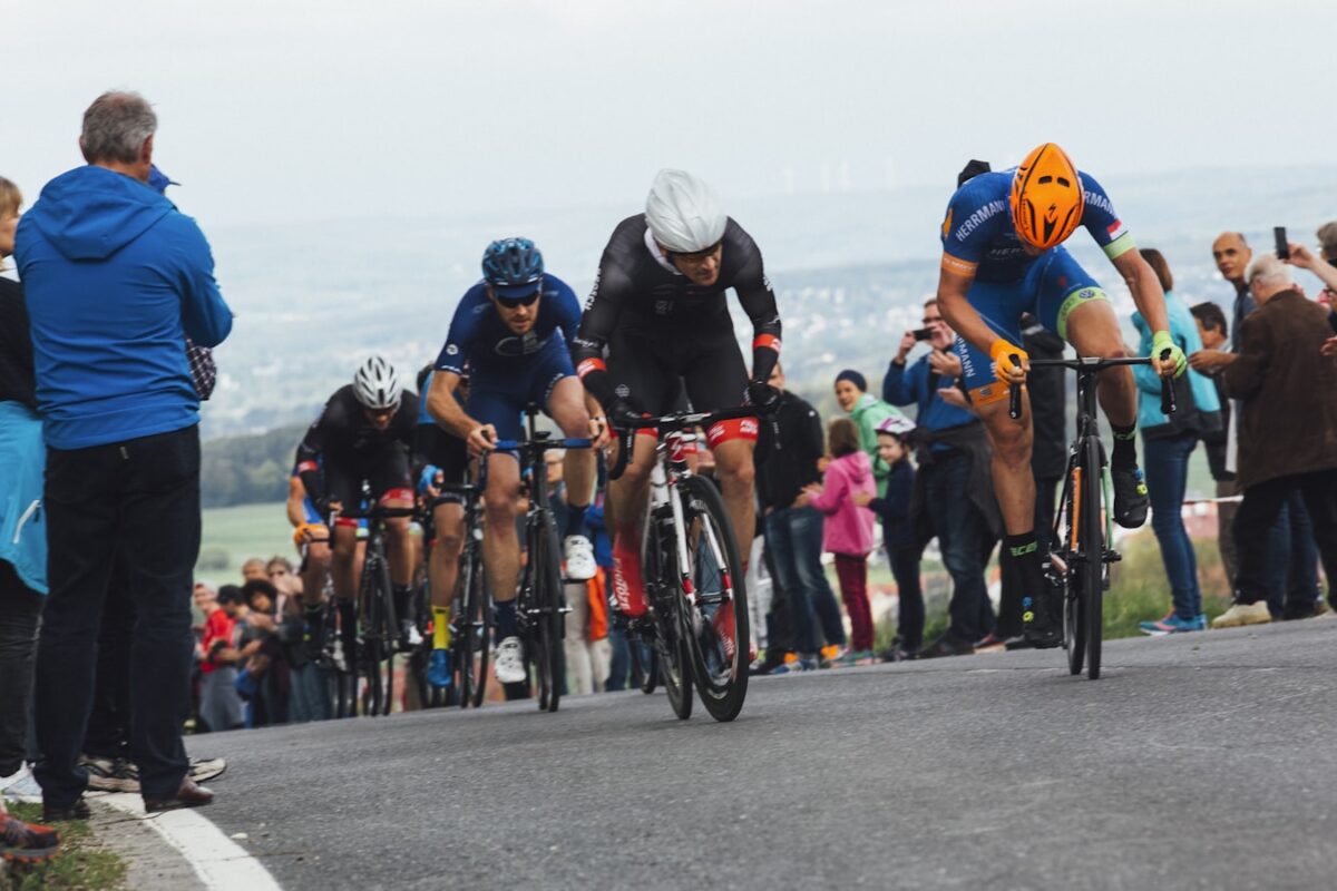 AI-generated illustration of a cyclist in a yellow jersey climbing a packed mountain stage finish on a winding alpine road surrounded by dense crowds of Tour de France spectators