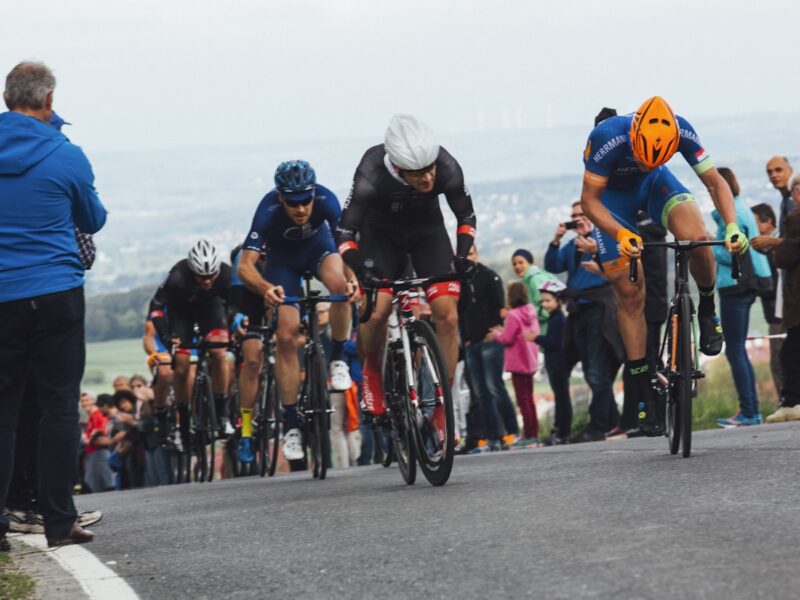 AI-generated illustration of a cyclist in a yellow jersey climbing a packed mountain stage finish on a winding alpine road surrounded by dense crowds of Tour de France spectators