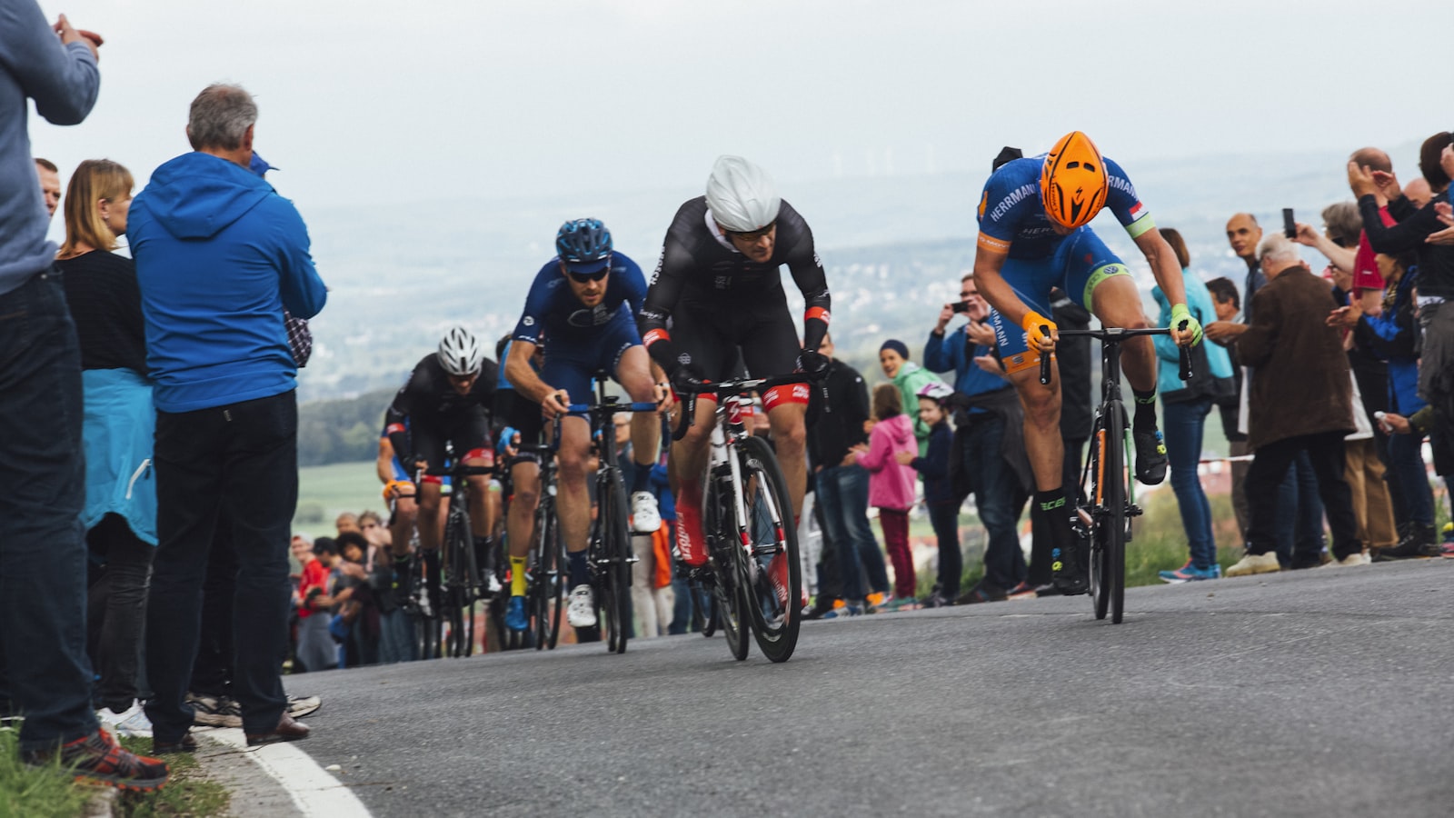AI-generated illustration of a cyclist in a yellow jersey climbing a packed mountain stage finish on a winding alpine road surrounded by dense crowds of Tour de France spectators