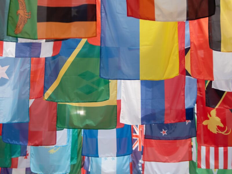 AI-generated illustration of a formal diplomatic negotiation room with national flags, an oval conference table and government documents under warm overhead lighting