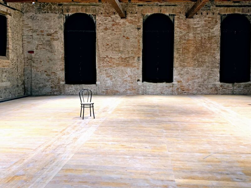 An empty small music venue before a show, with a dimly lit stage, cables and monitors in place and chairs stacked at the side