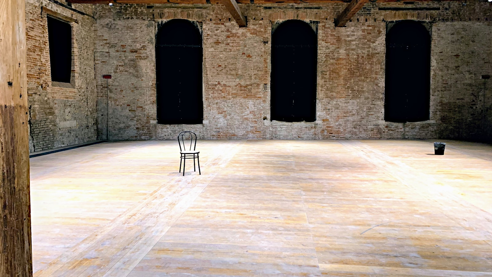 An empty small music venue before a show, with a dimly lit stage, cables and monitors in place and chairs stacked at the side